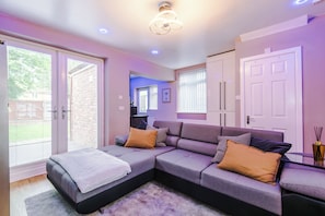Una sala de estar moderna con un sofá seccional, una cama pequeña y una mesa de centro de vidrio.