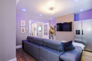 A modern living room with a sofa, a flat-screen TV, a refrigerator, and a wooden accent wall.