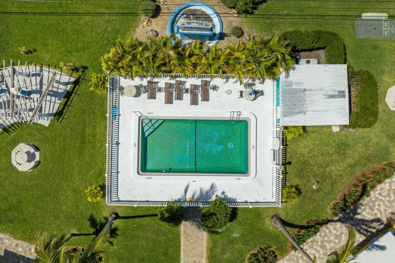 An aerial view of a swimming pool area with a rectangular pool, lounge chairs, and a covered seating area.