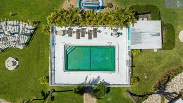 An aerial view of a swimming pool area with a rectangular pool, lounge chairs, and a covered seating area.