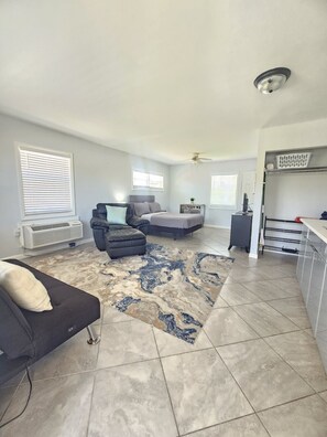 A living room with a sofa, a chair, a bed, a ceiling fan, and a kitchen area with a laundry basket. - Perfect location next to Ft Myers & Ft Myers Beach (Fort Myers)