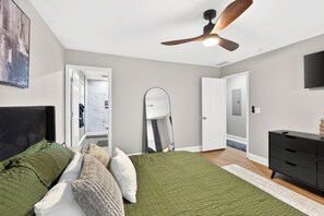 Une chambre à coucher comprenant un lit, un ventilateur de plafond, une commode et une porte donnant sur une autre pièce.