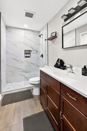 Une salle de bain avec un lavabo blanc, des meubles en bois, un mur en marbre et un espace douche.