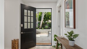 Un acceso a un patio con un banco de madera, una planta en maceta y un cuadro en la pared.