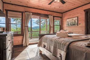 Ein Schlafzimmer einer Holzhütte mit einem großen Bett, einer Kommode und Blick auf eine bewaldete Landschaft durch große Fenster.