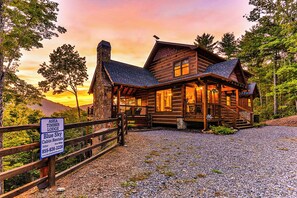 A log cabin lodge with a stone chimney, wooden deck, and a gravel driveway. - Aska Timber Lodge | Blue Ridge, GA (Cherry Log)