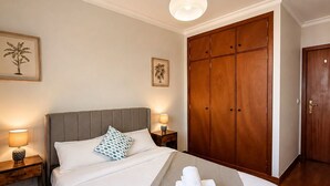 Quarto bem organizado com cama, abajures, guarda-roupa e luminária no teto.