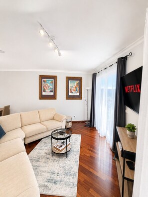 Un salón con sofá, mesa de centro, cuadros enmarcados, televisor y planta.