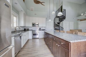 A kitchen with white cabinets, stainless steel appliances, a wooden island, and a black spiral staircase. - 1327 - Seaglass Retreat, Corolla Retreat | Hot Tub, Pool & 4BR Comfort (Corolla)