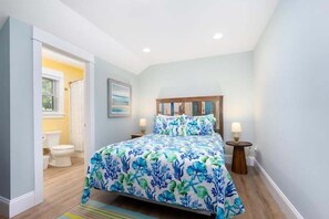 A bedroom with a bed, a nightstand, a bedside table, a window, and a door leading to a bathroom. - 1327 - Seaglass Retreat 4BR Oceanside townhouse in Corolla with pool, grill, and beach access. (Corolla)