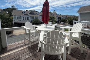 A wooden deck with white Adirondack chairs and a table, overlooking a residential area with houses. - 1327 - Seaglass Retreat 4BR Oceanside townhouse in Corolla with pool, grill, and beach access. (Corolla)