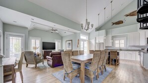 A spacious living area with a dining table, chairs, a sofa, and a TV. - 1327 - Seaglass Retreat, Corolla Retreat | Hot Tub, Pool & 4BR Comfort (Corolla)