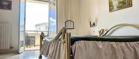 Una habitación con una cama, una ventana con cortinas, un cuadro en la pared y vistas al exterior.