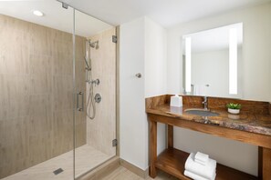 Ein modernes Badezimmer mit einer gläsernen Dusche, einem Holzkosmetikschrank und einem großen Spiegel.