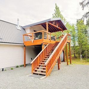 A wooden deck with a staircase leading to a covered area, a garage door, and a gravel driveway.