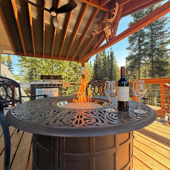 A patio with a decorative metal table, a fire feature, a wine bottle, and a grill.