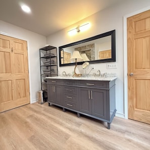 A bathroom with a vanity, a mirror, a shelf with towels, and wooden doors.