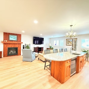 A spacious living area with a fireplace, a television, a chandelier, and a kitchen island.