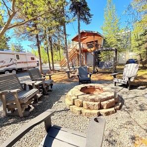 En campingplats med en eldstad, träbänkar och ett avskärmat sittområde.