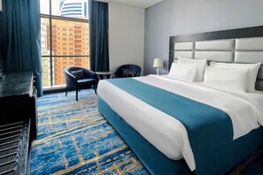 Ein Hotelzimmer mit einem großen Bett, einem Schreibtisch, einem Stuhl und Blick auf Gebäude durch das Fenster.