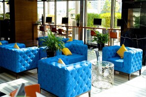Eine moderne Lobby mit blauen Sofas, einem Glastisch und großen Fenstern.