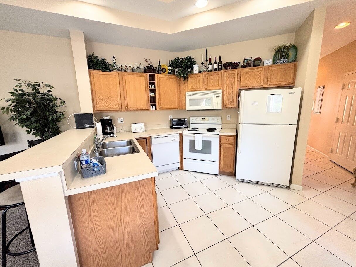 A modern kitchen with wooden cabinets, a built-in microwave, a refrigerator, and a small island with a sink.