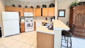 A kitchen with wooden cabinets, a white refrigerator, a microwave, a stove, and a sink. - Right Direction Rentals 2 Bedroom Villa 8231 (Port St. Lucie)
