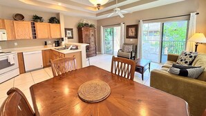 A spacious kitchen with wooden cabinets, a dining table with chairs, a ceiling fan, and a view to a balcony. - Right Direction Rentals 2 Bedroom Villa 8231 (Port St. Lucie)