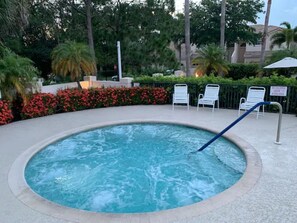 Un bain à remous entouré d’une piscine, avec un panneau indiquant que l’accès à l’espace spa est interdit aux enfants de moins de 15 ans.