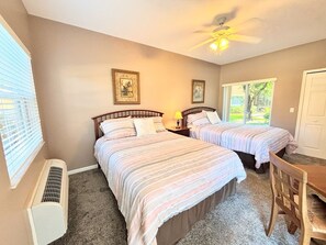 Une chambre avec deux lits, un ventilateur de plafond, une fenêtre avec des stores et un radiateur.