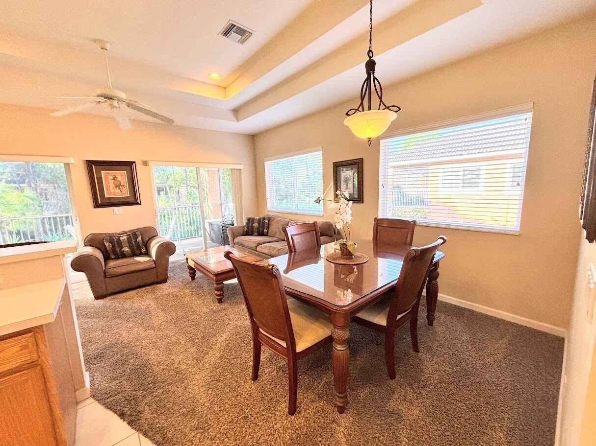 A dining area with a table and chairs, a ceiling fan, and large windows.