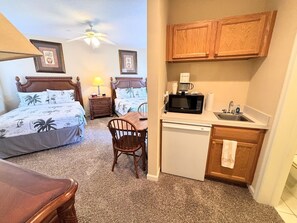 A hotel room with two beds, a desk, a chair, a microwave, a sink, and wooden cabinets. - Right Direction Rentals Studio Villa 8255 (Port St. Lucie)