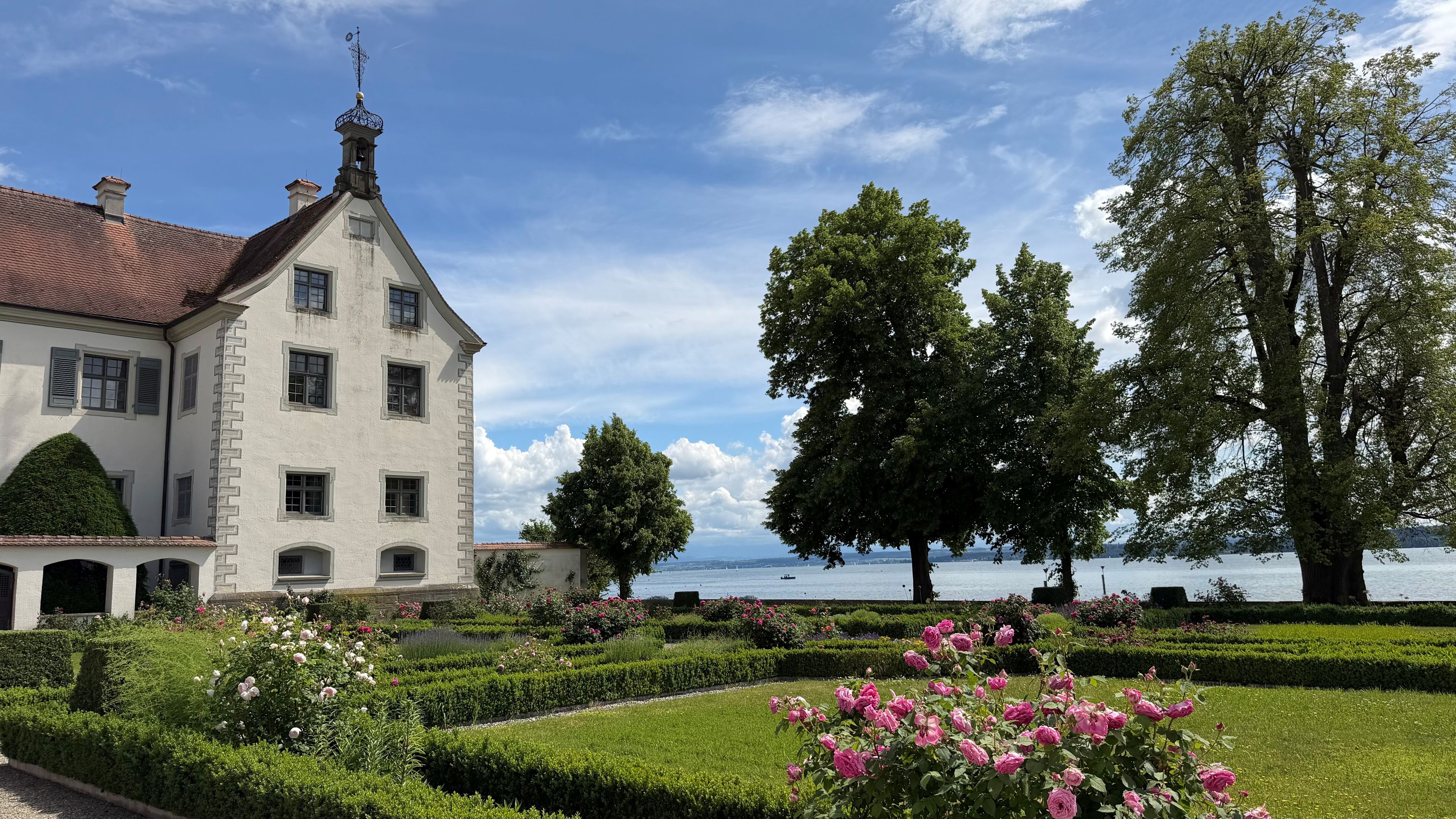 Un grande edificio con facciata simmetrica, un ingresso centrale e un giardino curato con rose e siepi.