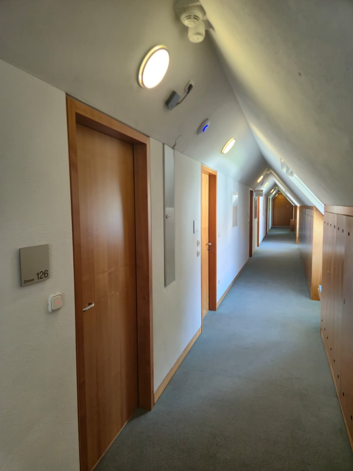 A corridor with wooden doors, a light switch, and a thermostat on the wall.