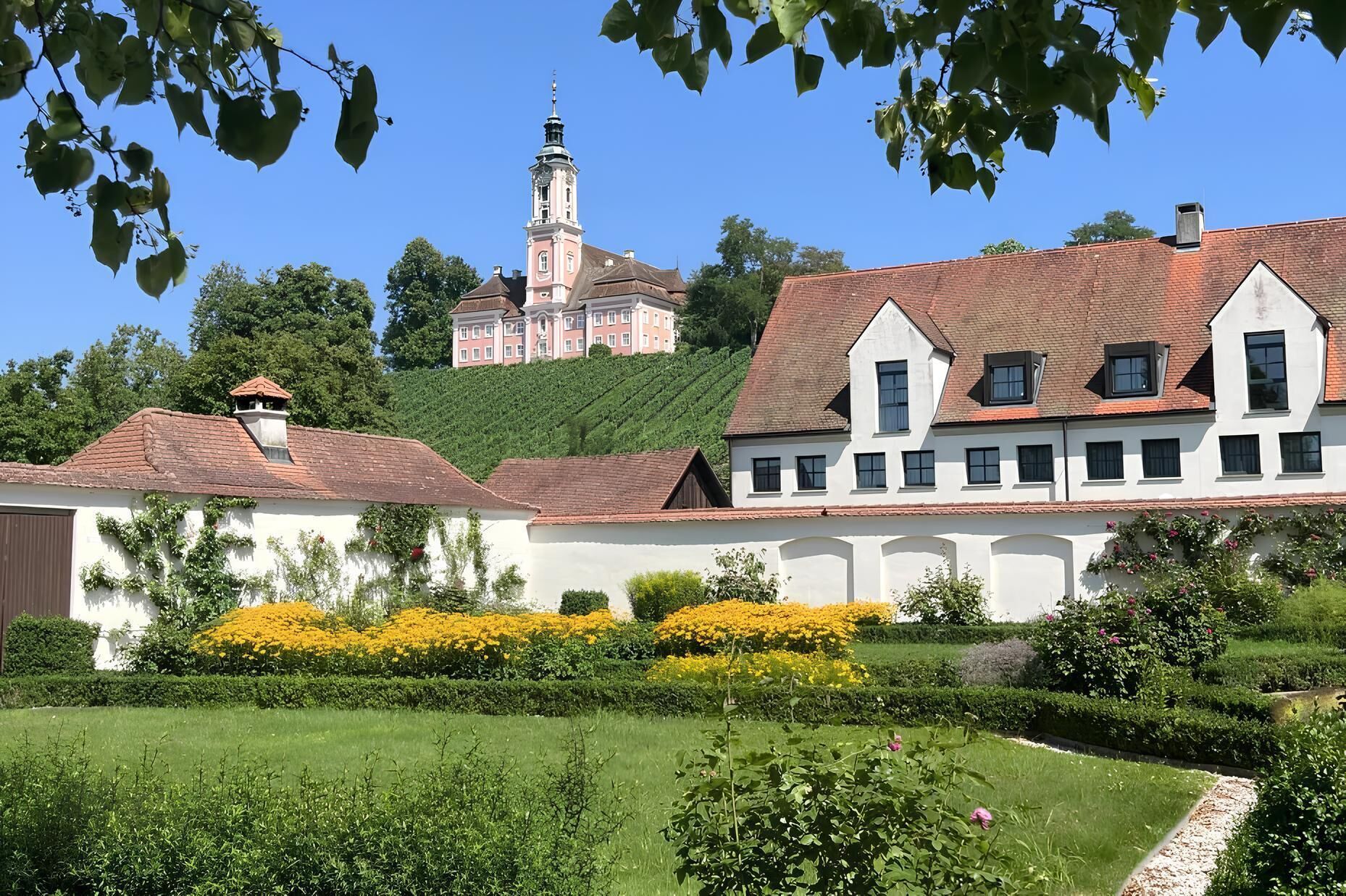 Un bâtiment doté d’une tour imposante, entouré de jardins luxuriants et situé au pied d’une colline.