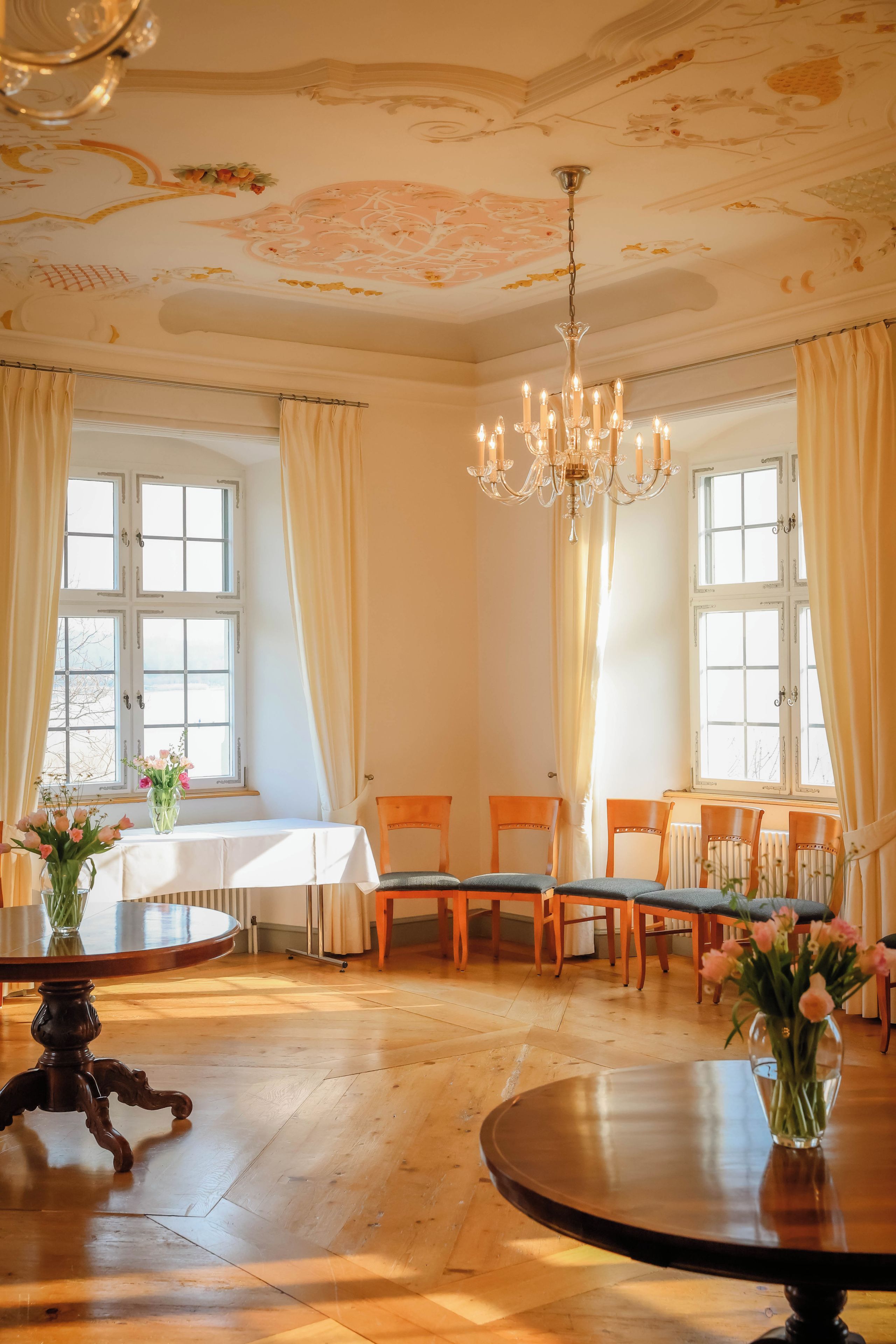 A dining room with a chandelier, wooden chairs, a round table, and a window with curtains.