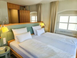 Habitación de hotel con cama doble, lámparas de noche, mesita de noche, espejo y ventana con cortinas.
