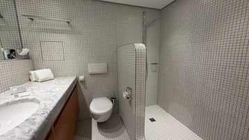 A modern bathroom with a marble sink, a toilet, and a glass-enclosed shower.