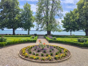 Un jardín ajardinado con un sendero de grava que conduce a un parterre circular, rodeado de setos y árboles cuidadosamente podados.