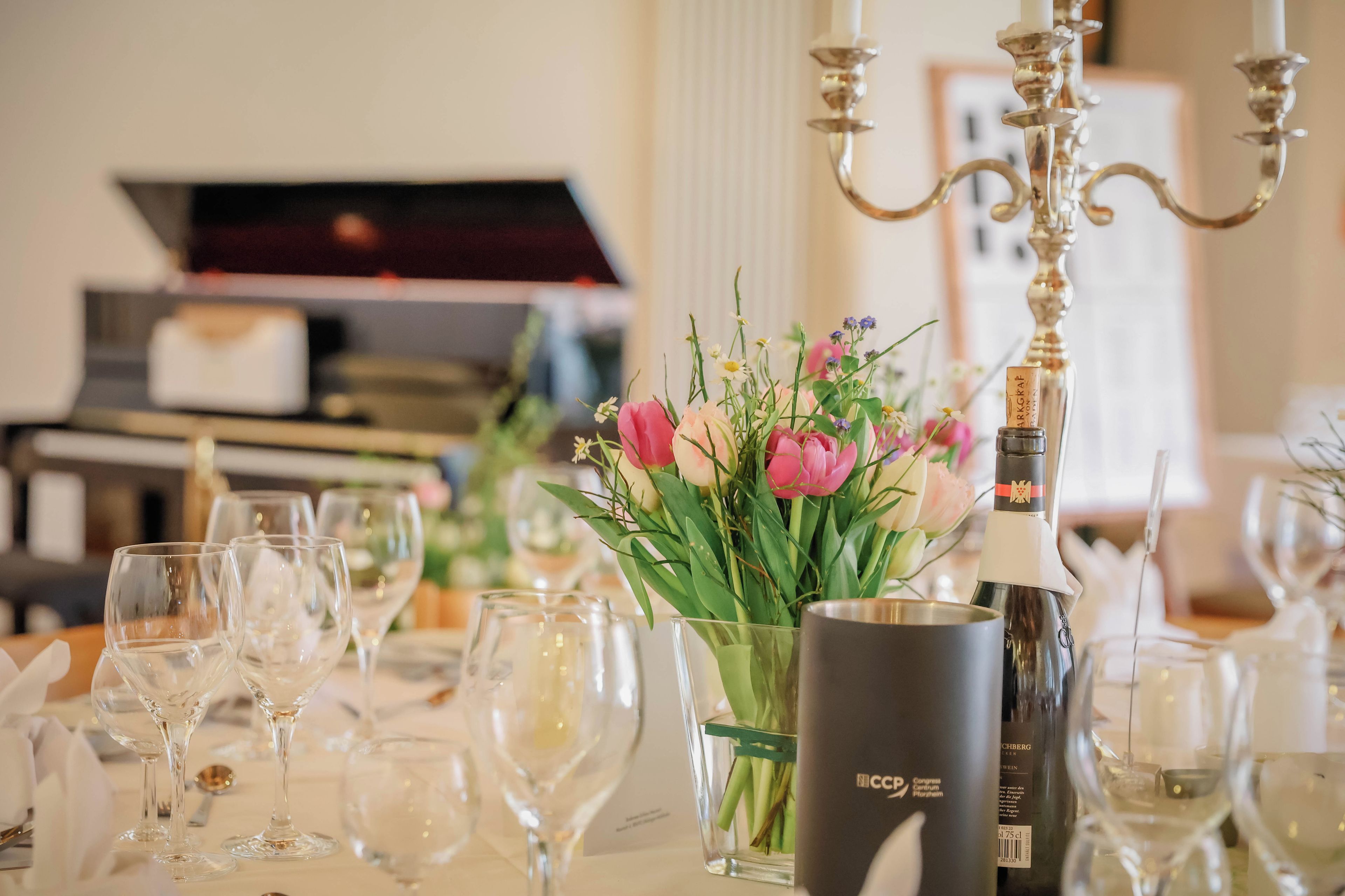 Une table dressée pour un événement formel, avec des verres à vin vides, un vase rempli de fleurs et une bouteille de champagne.