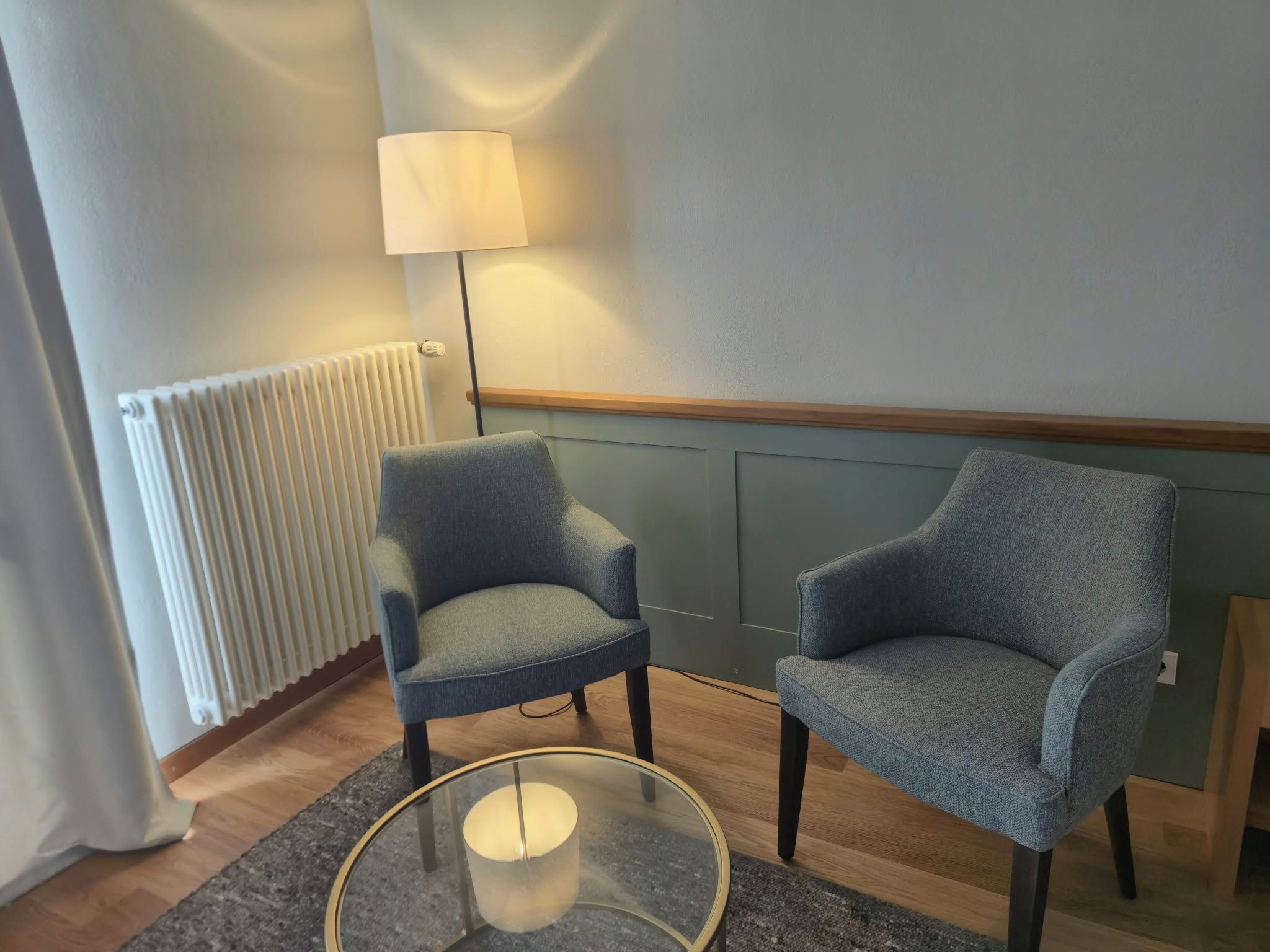 A room with two armchairs, a floor lamp, and a glass table.