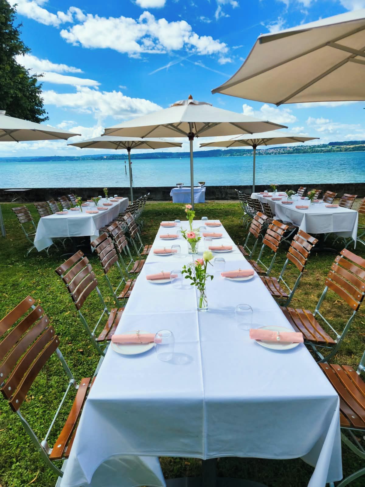 An outdoor dining area with tables set for a meal, overlooking a body of water.