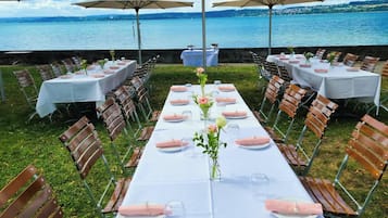 An outdoor dining area with tables set for a meal, overlooking a body of water.