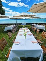 Un área de comedor al aire libre con mesas dispuestas para una comida, con vistas a un cuerpo de agua.