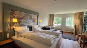 Habitación de hotel con dos camas, un cuadro grande en la pared y vistas a árboles a través de las ventanas.