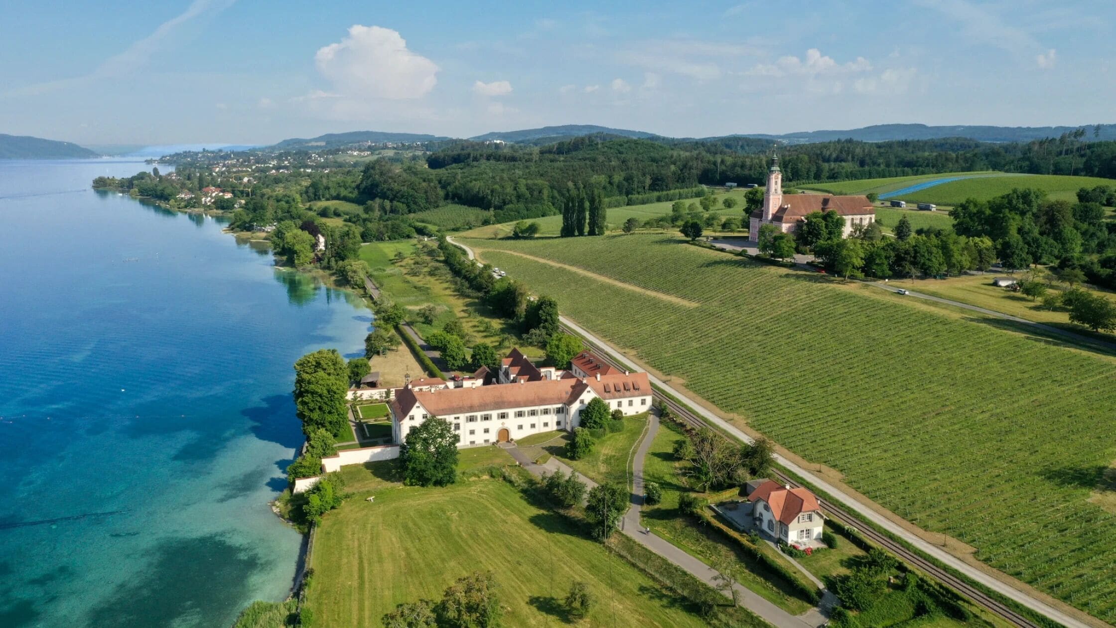 Vista aérea de una extensa propiedad con un lago, viñedo e iglesia.