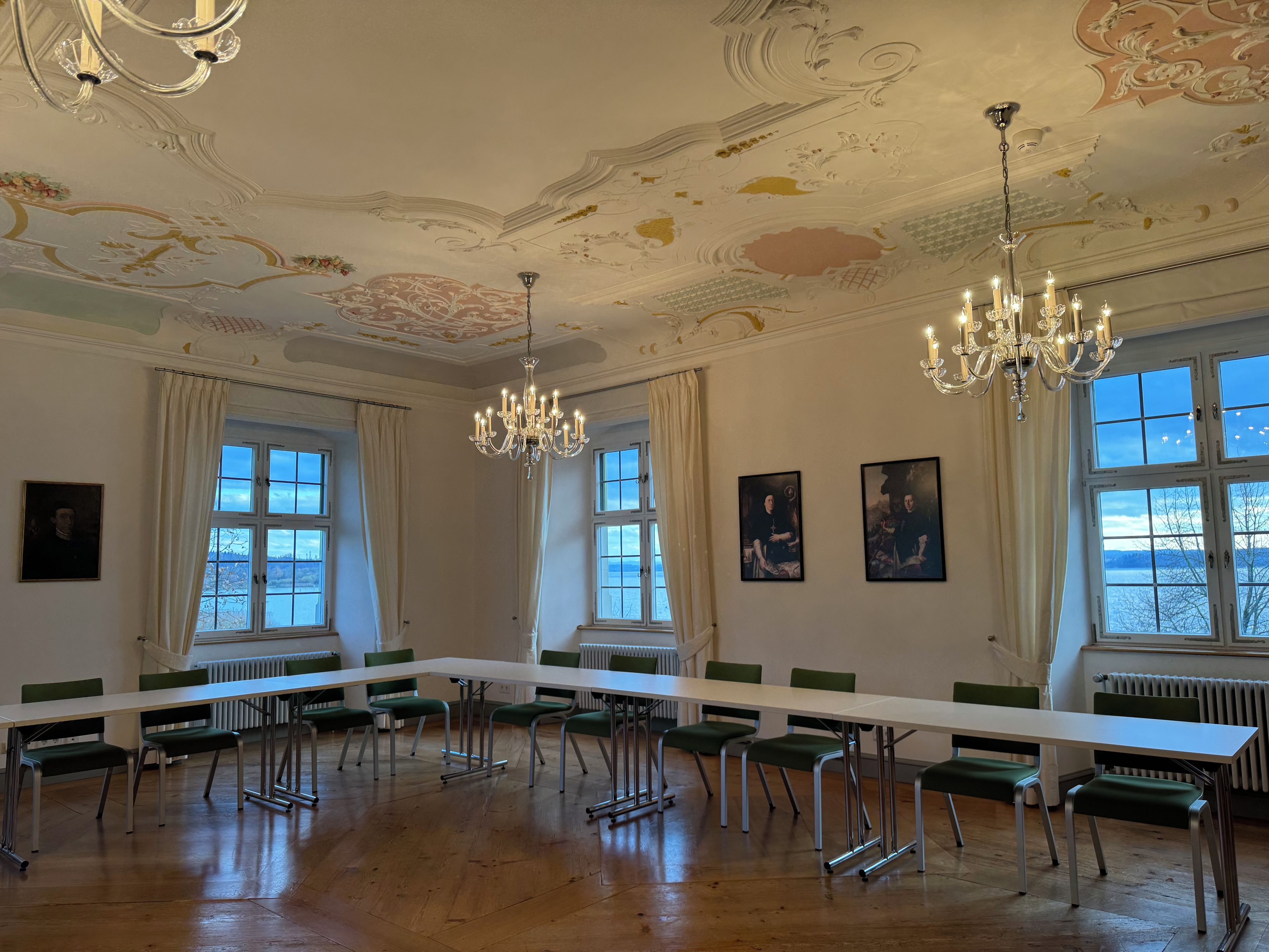 Una sala conferenze con un lungo tavolo, sedie, lampadari e ampie finestre con vista.