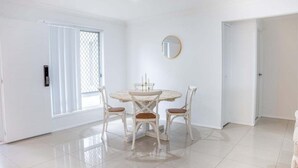 A room with a round dining table, four chairs, a round mirror on the wall, and a sliding glass door. - 4BR Luxury Retreat (Gold Coast)