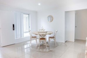 A room with a round dining table, four chairs, a round mirror on the wall, and a sliding glass door. - 4BR Luxury Retreat (Gold Coast)