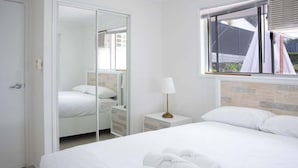 A hotel room with a bed, a nightstand, a lamp, a window, and a mirror. - 4BR Luxury Retreat (Gold Coast)